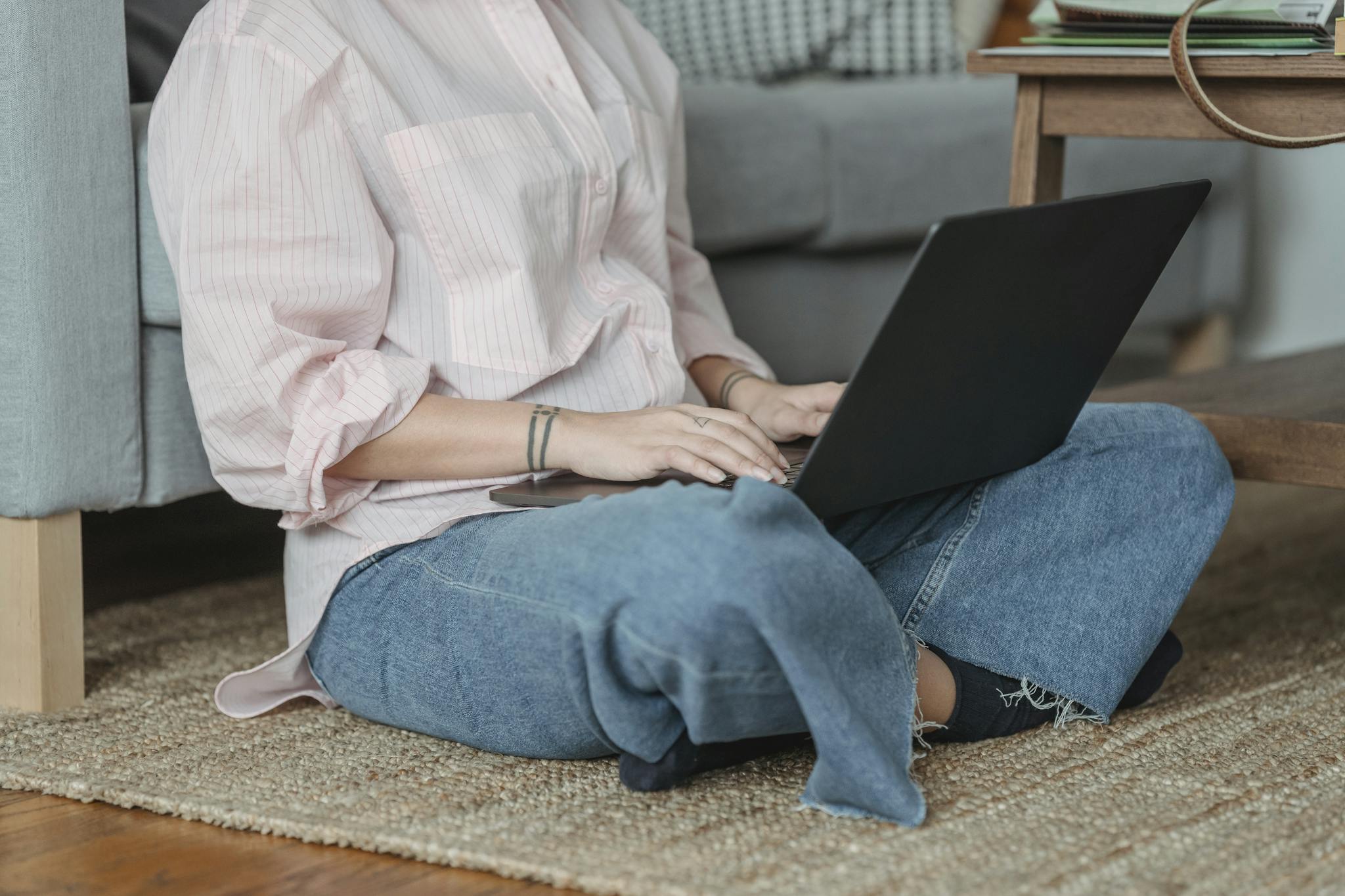 Crop unrecognizable female freelancer sitting on floor and browsing netbook in living room in daytime